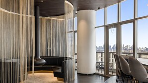 A modern interior with a curved black sofa, a round table with chairs, and a view of the cityscape through large windows.