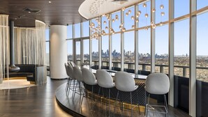 A modern bar area with a city view, featuring a curved counter, multiple bar stools, and hanging spherical light fixtures.