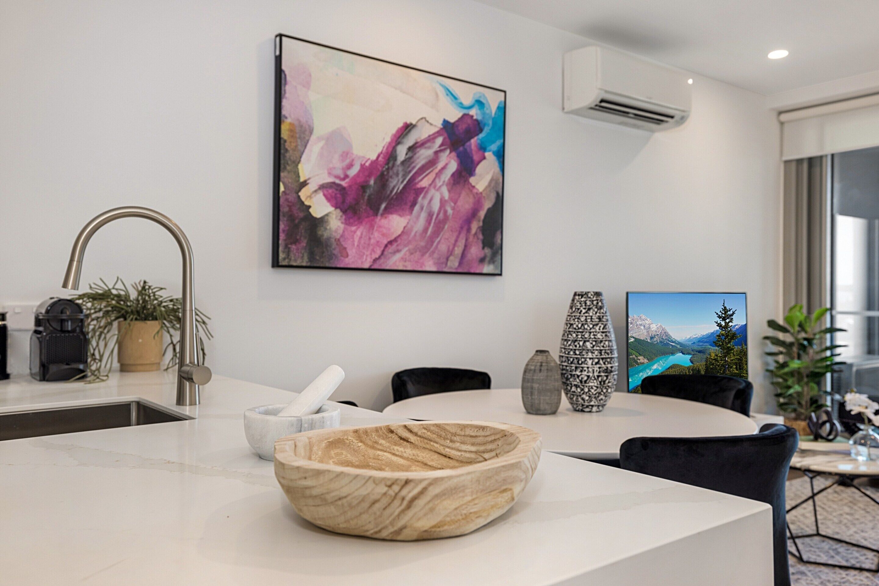 Uma cozinha moderna com bancada de mármore, uma tigela de madeira, uma pintura e uma área de jantar com vista para montanhas.