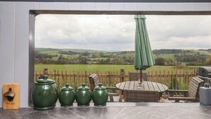 A patio area with a view of rolling hills, a wooden fence, and a green umbrella.