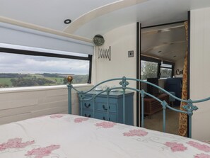 A bedroom with a bed, a dresser, and a view of the countryside. - The Bus on the Hill (Tiverton)
