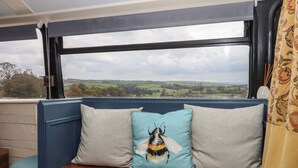 A bench with cushions and a view of a countryside landscape. - The Bus on the Hill (Tiverton)