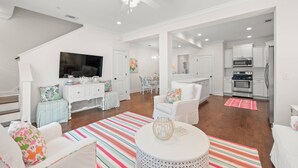 A spacious living room with a flat-screen TV, white furniture, and a staircase leading to another level. - Pool | Pet Friendly | Clean & Bright | Patio | Grill | Great Kitchen | Beach Chairs (St. Simons Island)