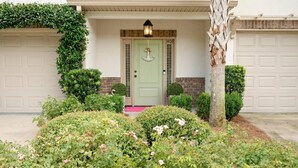 A house with a green door, a porch with a lantern, and a garage door. - Pool | Pet Friendly | Clean & Bright | Patio | Grill | Great Kitchen | Beach Chairs (St. Simons Island)