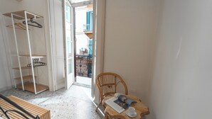 Una stanza con una sedia di legno, un tavolo con una rivista e una tazza, una panca di legno e una porta bianca che dà su un balcone.