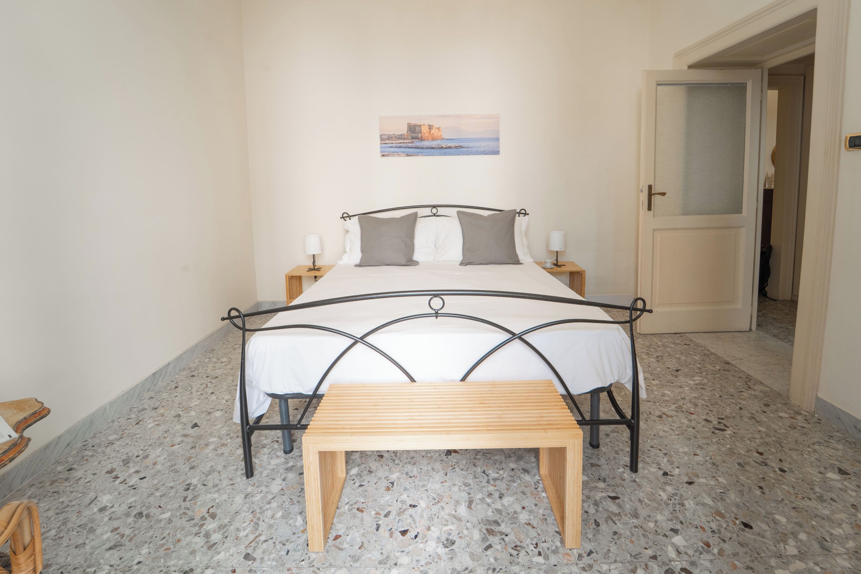 A bedroom with a bed, bedside tables, a bench, and a painting on the wall.