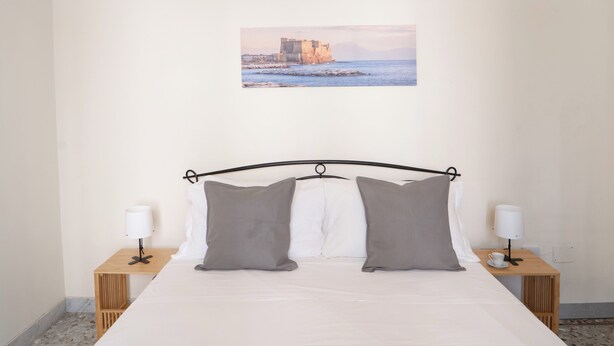Una camera da letto ordinata con un letto, due comodini e un quadro appeso alla parete raffigurante una scena costiera.