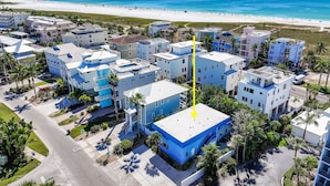 Vista aérea de una zona residencial costera con edificios modernos, una playa al fondo y una flecha amarilla señalando un edificio en particular.
