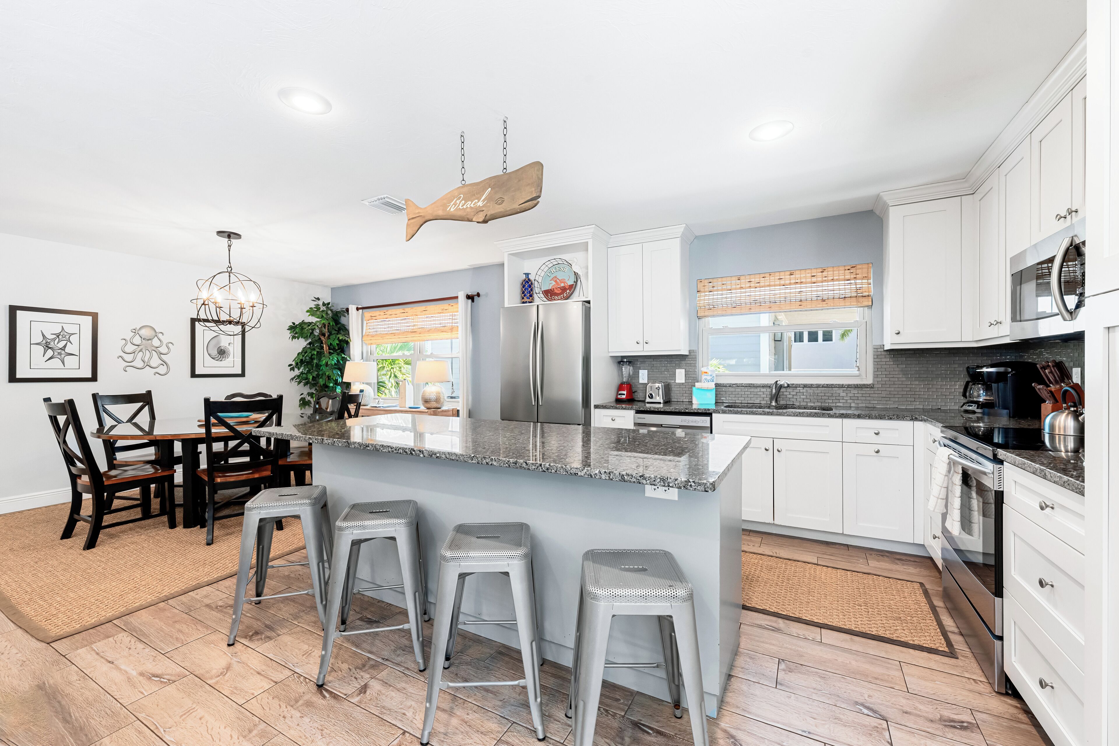 A modern kitchen with white cabinets, a large island with bar stools, stainless steel appliances, and a hanging fish decoration.