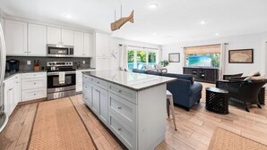 Une cuisine moderne avec des meubles blancs, un îlot central, un four à micro-ondes et un four traditionnel. On y trouve également un coin repas avec un canapé bleu et des meubles en osier.