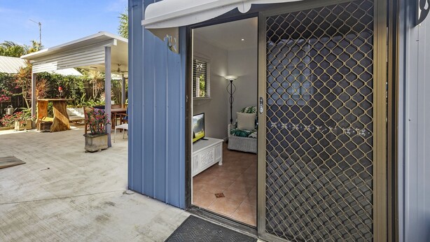 A modern house with a sliding glass door leading to a living area with a sofa, a TV, and a lamp. - The Little Blue Shack - Marcoola Granny Flat (Sunshine Coast)