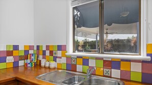 A kitchen with a colorful tile backsplash, a window with a view of the outside, and a stainless steel sink. - The Little Blue Shack - Marcoola Granny Flat (Sunshine Coast)