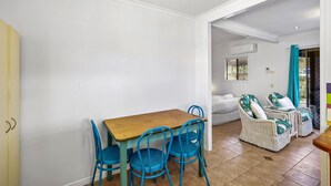 A dining area with a wooden table and blue chairs, a white sofa, and wicker chairs with cushions. - The Little Blue Shack - Marcoola Granny Flat (Sunshine Coast)