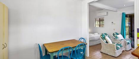 A dining area with a wooden table and blue chairs, a white sofa, and wicker chairs with cushions.