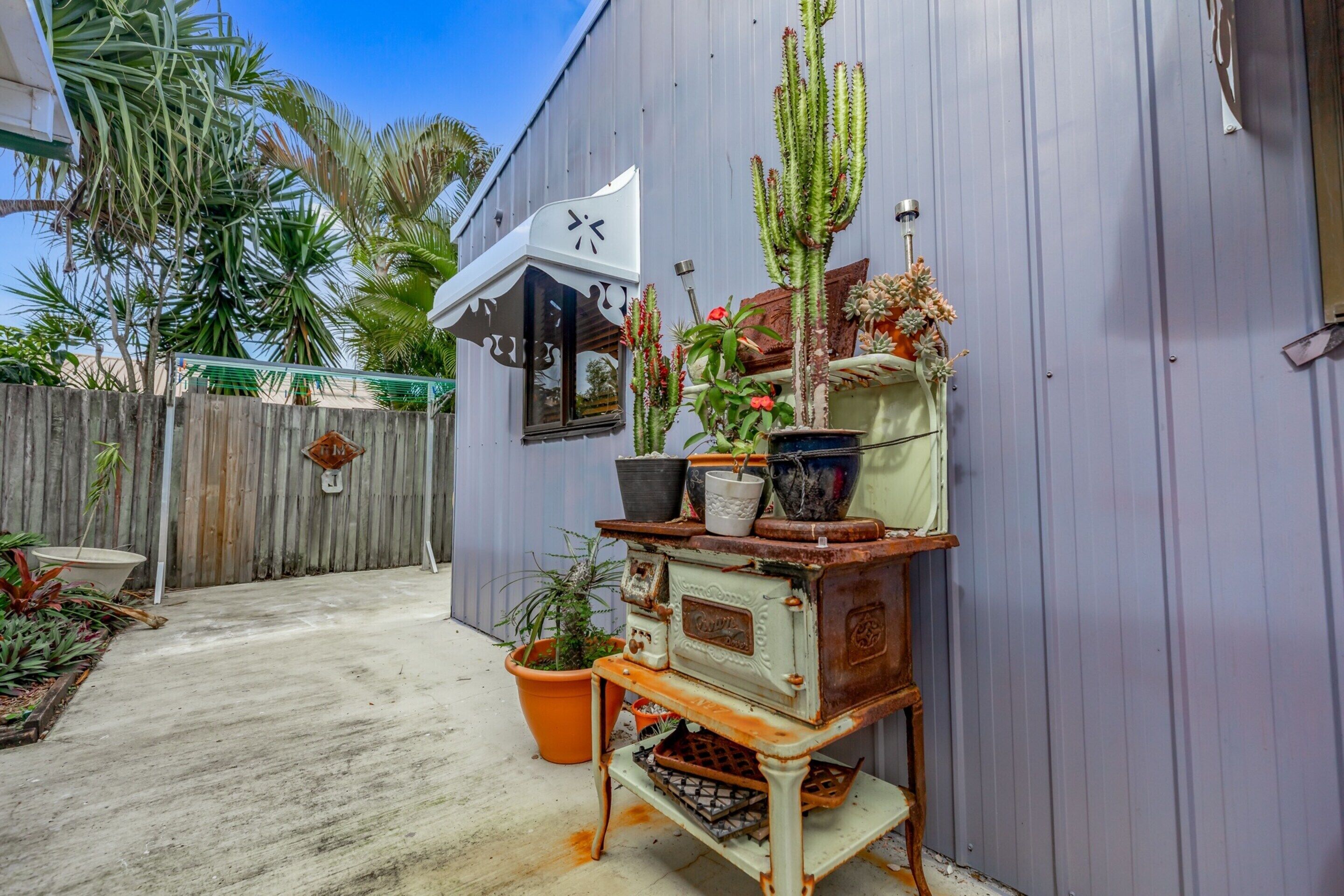 A rustic outdoor area with a vintage stove, potted plants, and a wooden fence.