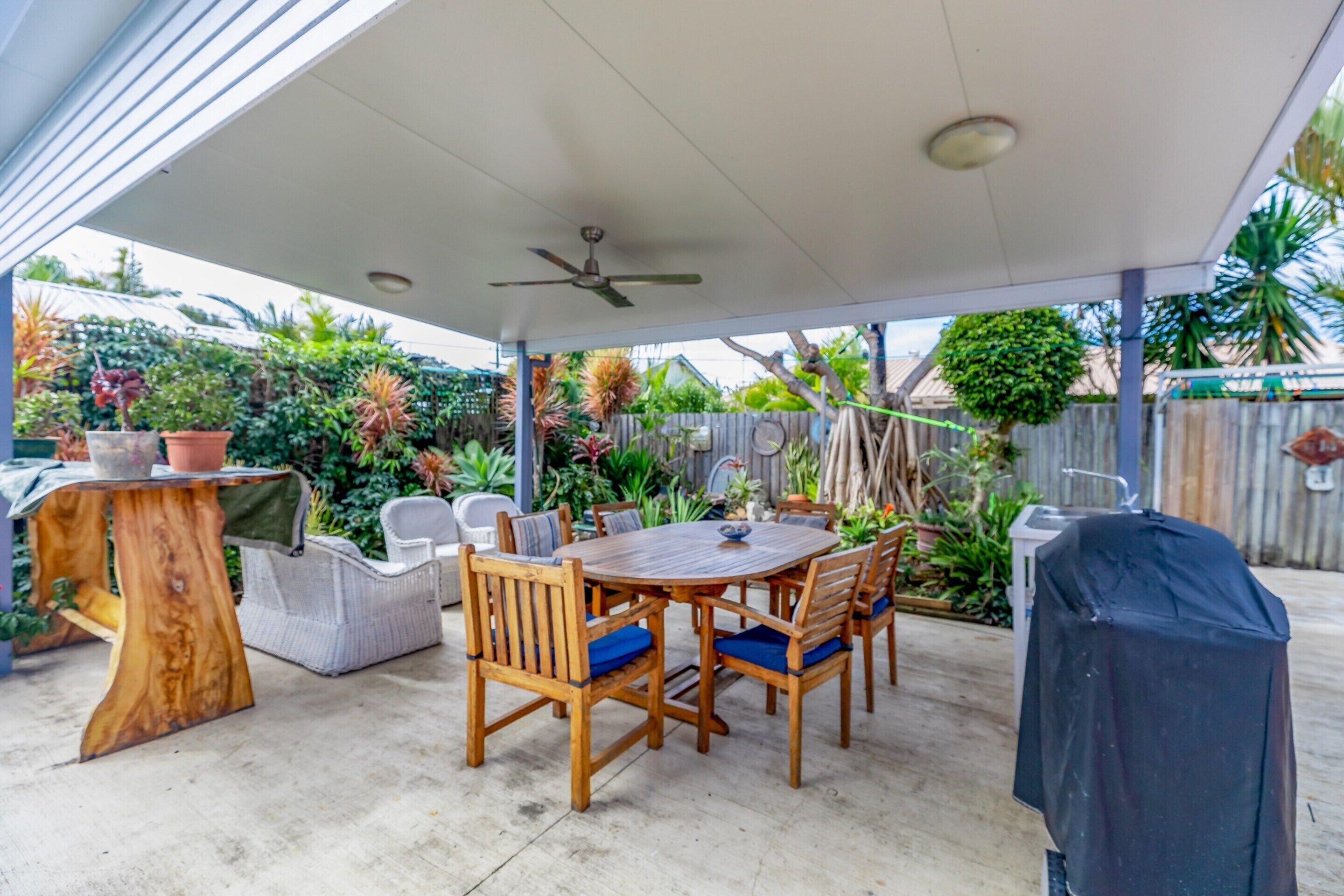 An outdoor patio with a round wooden table and chairs, surrounded by potted plants and a wooden fence.