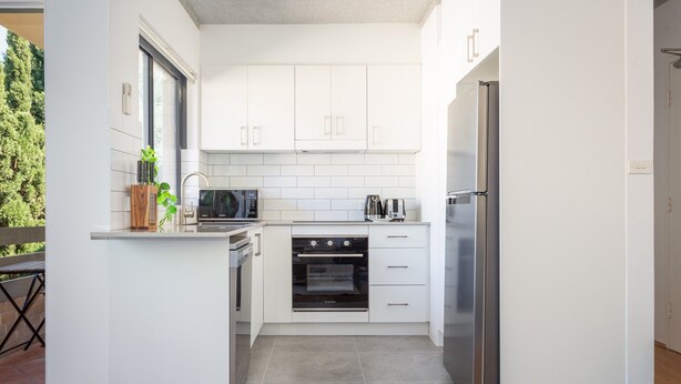 Una cucina moderna con mobili bianchi, un frigorifero in acciaio inossidabile, un forno integrato e un microonde.