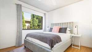 Una camera da letto con un letto, un comodino, una finestra con tende e una ventola a soffitto.