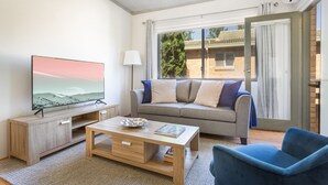 Un soggiorno moderno con una televisione a schermo piatto, un tavolino in legno, un divano con cuscini e una poltrona blu.