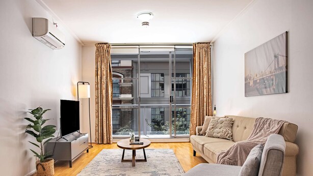 A modern living room with a sofa, a TV, a coffee table, and a large window with curtains. - Stylish Studio With Pool & Gym in Heart of Sydney (Sydney)