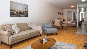 A modern living room with a sofa, armchair, and coffee table. There is a painting on the wall and a dining area in the background. - Stylish Studio With Pool & Gym in Heart of Sydney (Sydney)