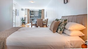 A hotel room with a large bed, a dining area with chairs, and a view of the outside. - Stylish Studio With Pool & Gym in Heart of Sydney (Sydney)
