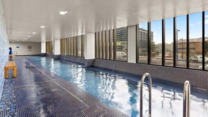 An indoor swimming pool with clear glass walls, a tiled floor, and a wooden bench. - Chic 1-bed With Pool by River, Ferry & Amenities (Sydney)