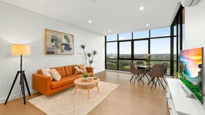 A modern living room with a large window, a sofa, a coffee table, and a TV. - Chic 1-bed With Pool by River, Ferry & Amenities (Sydney)