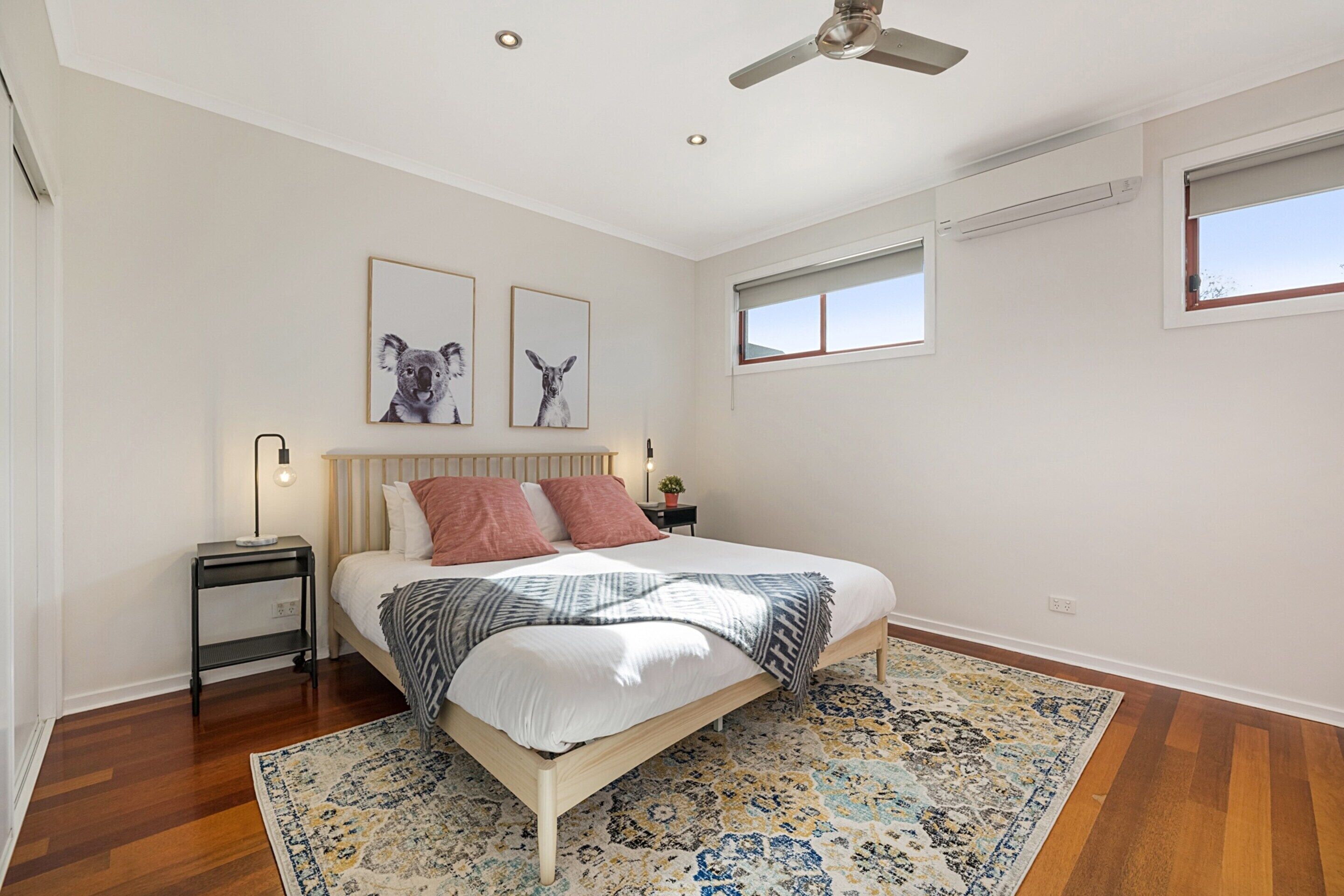 Un dormitorio con cama, mesita de noche, ventilador de techo y cuadros en la pared.