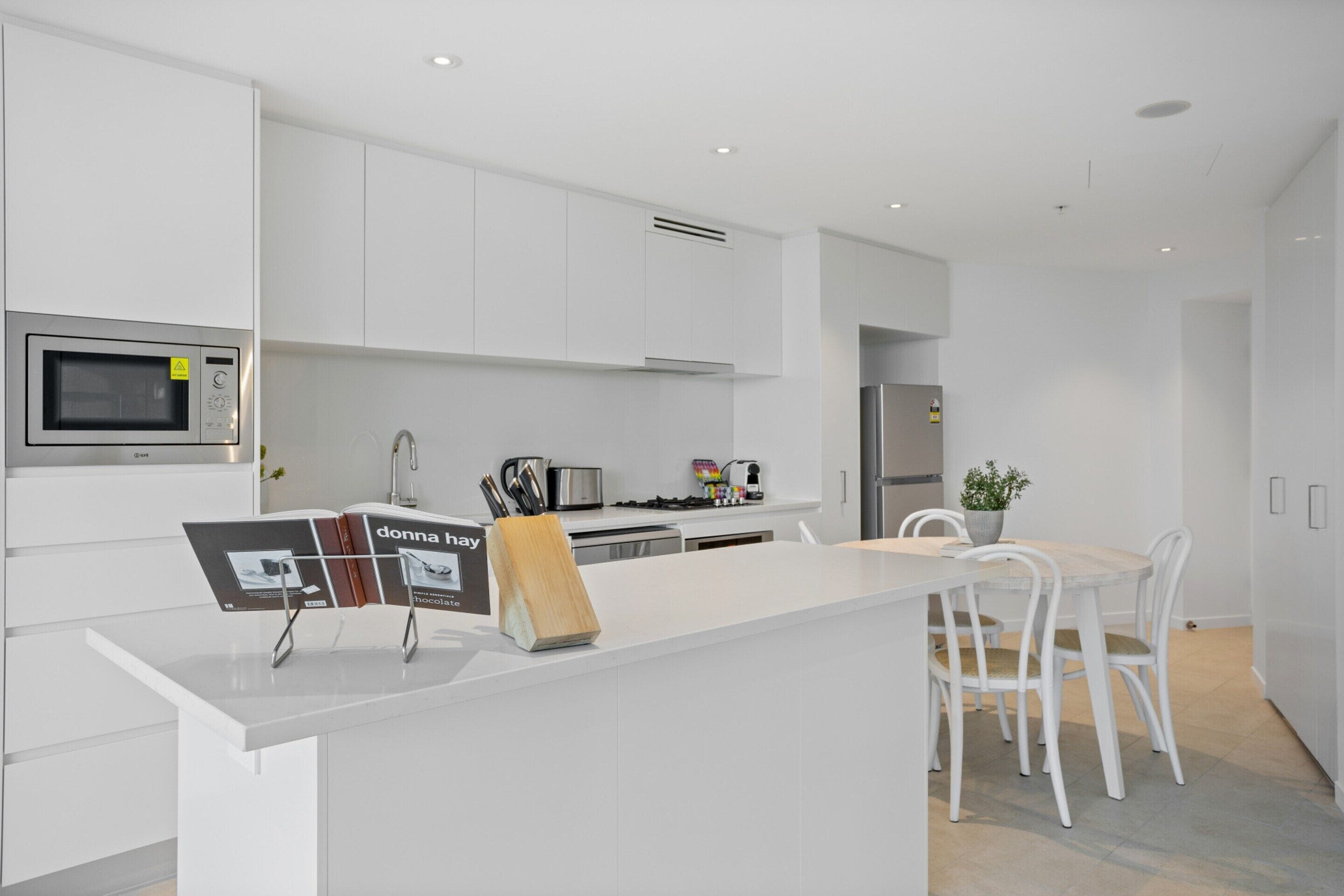 A modern kitchen with white cabinetry, a central island, and a dining area with white chairs.
