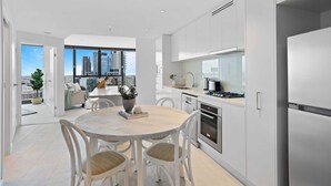 A modern kitchen with white cabinets, stainless steel appliances, and a dining area with a round table and chairs. - Breathtaking City Views 1-bed With Pool, BBQ & Gym (Brisbane)
