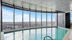 A large indoor swimming pool with a city view through large windows. - Breathtaking City Views 1-bed With Pool, BBQ & Gym (Brisbane)