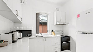 Une cuisine moderne avec des meubles blancs, un four encastré, un  évier et une fenêtre donnant sur une façade en briques.