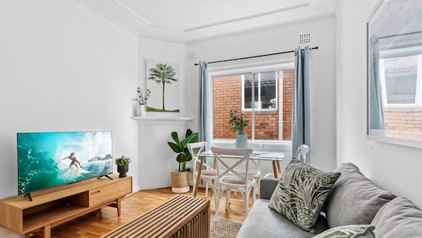 Un salon moderne avec un meuble de rangement en bois pour les appareils électroniques, un canapé gris et un coin repas avec des chaises blanches et une table.