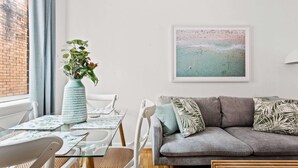 Un salon moderne avec un canapé gris, une table basse en verre et un tableau représentant une plage, encadré et accroché au mur.