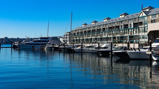 A marina with several boats docked, a building with multiple balconies, and a clear blue sky. - Inner-city Apartment Minutes Walk to Dining Hubs (Sydney)