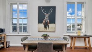 A dining area with a wooden table, four chairs, a potted plant, and a painting of a deer on the wall. - Inner-city Apartment Minutes Walk to Dining Hubs (Sydney)