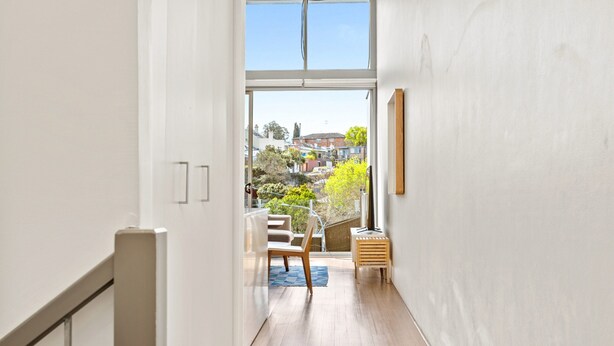 A narrow hallway leading to a balcony with a view of a residential area. - Charming Modern Apartment With City Views (Sydney)