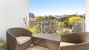 A balcony with wicker furniture and a view of a residential area. - Charming Modern Apartment With City Views (Sydney)