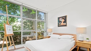 A bedroom with a large window, a bed, two bedside tables with lamps, and a framed picture on the wall. - Charming Modern Apartment With City Views (Sydney)