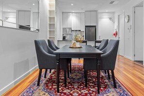 Un espace repas comprenant une table rectangulaire, quatre chaises grises et un tapis rouge à motifs.