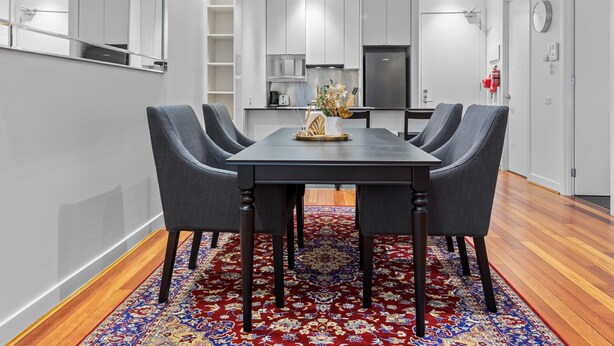 A modern dining area with a rectangular table, four grey chairs, and a red patterned rug. - Stylish and Spacious 2-bed Apartment Melbourne (Melbourne)