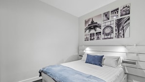 Ein modernes Schlafzimmer mit einem großen Bett, einem Kopfteil mit integrierter Beleuchtung und einer Wand, die mit Schwarz-Weiß-Kunstwerken zum Thema Paris geschmückt ist.