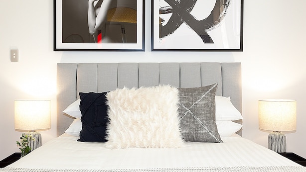A neatly made bed with a grey headboard, flanked by two bedside lamps, and framed artwork above. - Charming Studio With Balcony in Inner-city Glebe (Sydney)