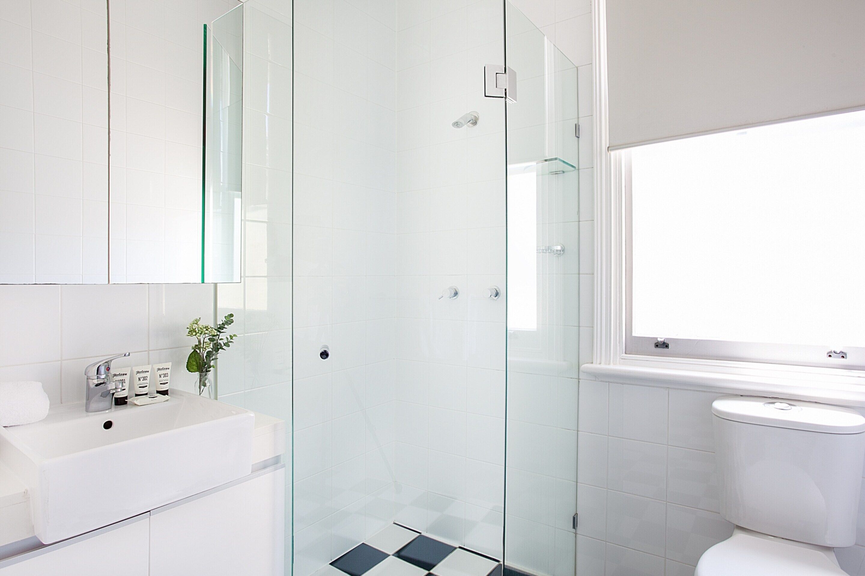 Un baño moderno con ducha de mampara de vidrio, lavamanos blanco y retrete.