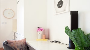 A modern room with a white desk, a clock, a framed picture, a black speaker, and a large green plant. - Charming Studio With Balcony in Inner-city Glebe (Sydney)