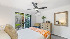 A bedroom with a bed, a ceiling fan, a dresser, a mirror, and a view of the outside. - Trendy 2-bed Home With Outdoor Entertainment (Sunshine Coast)