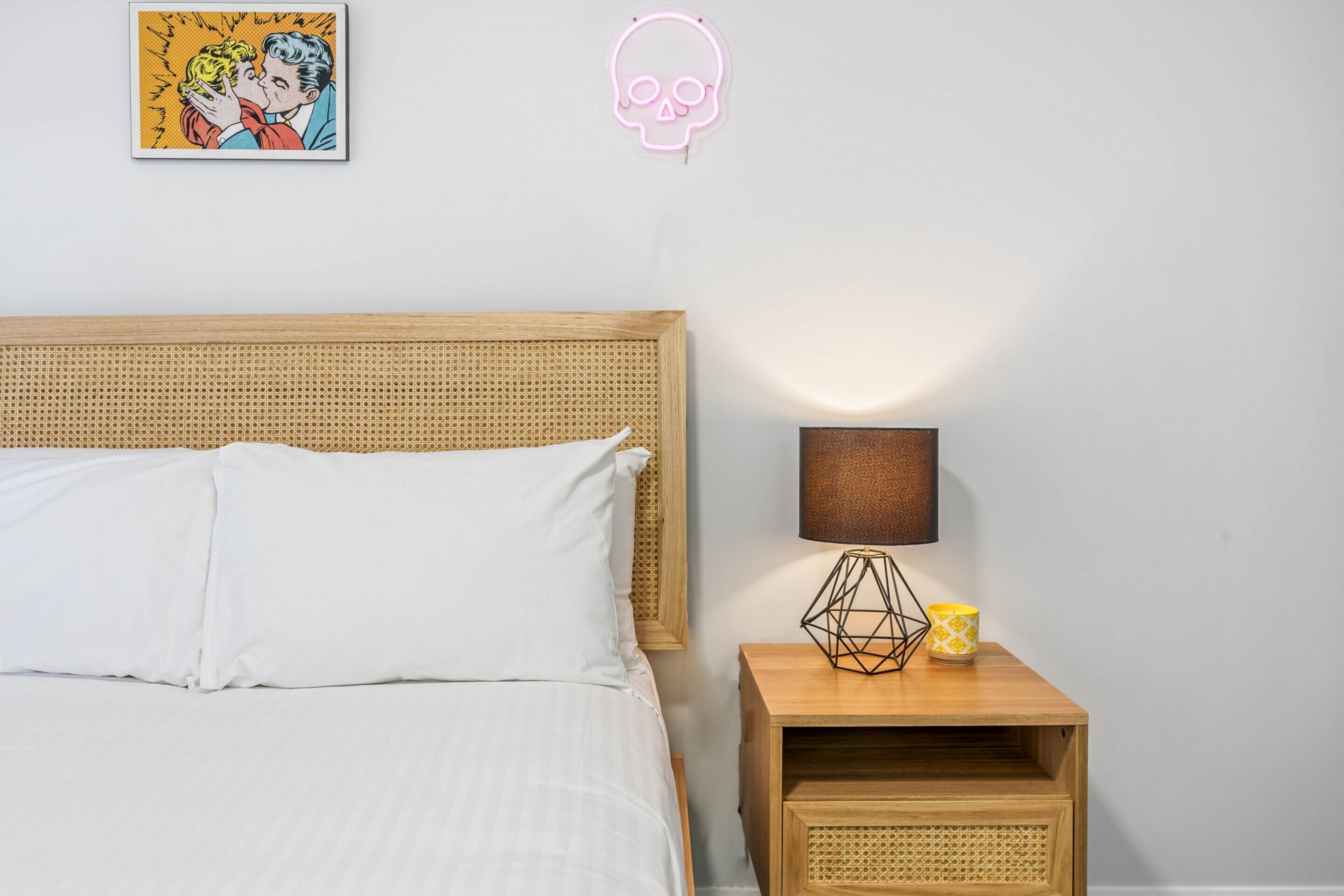A bedroom with a wooden headboard, a bedside lamp, and a framed comic book on the wall.