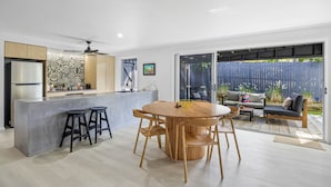 A modern kitchen with a central island, bar stools, and a dining area with a round table and chairs. - Trendy 2-bed Home With Outdoor Entertainment (Sunshine Coast)