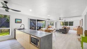 A modern kitchen with a central island, a dining area with a round table, and a living room with a sofa and chairs. - Trendy 2-bed Home With Outdoor Entertainment (Sunshine Coast)